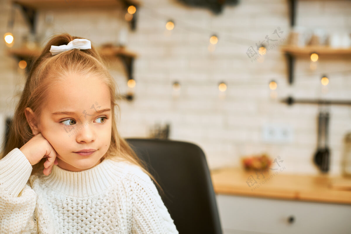 孩子一个七岁的女孩 穿着温暖舒适的毛衣 独自在家度过寒冷的冬天 手放在下巴下 脸上露出愁眉苦脸的表情 目光移开了小可爱快乐