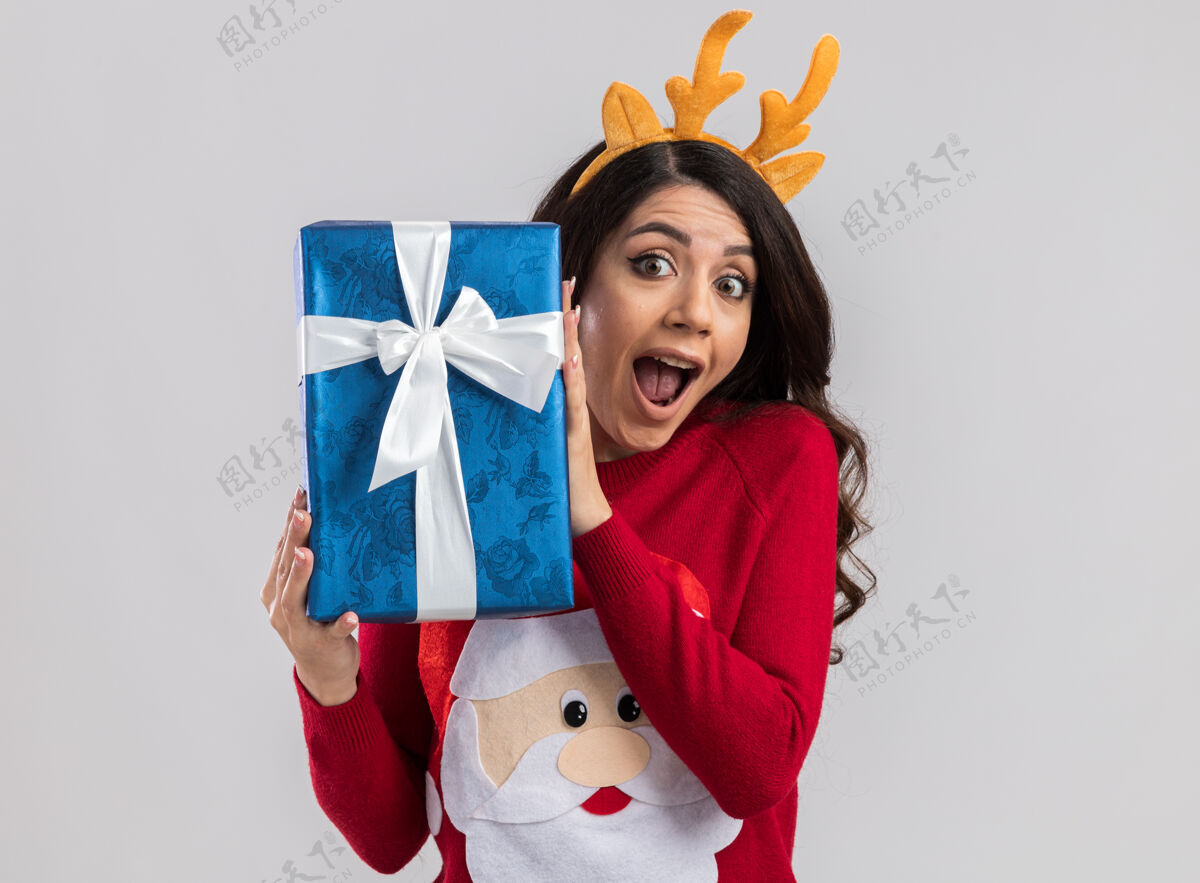 头带印象深刻的年轻漂亮女孩穿着驯鹿鹿角头带和圣诞老人毛衣拿着圣诞礼物包看快乐漂亮复制