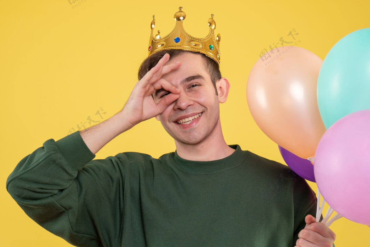 气球正面图戴着皇冠的帅哥拿着气球在黄色的眼睛前面放着奥基标志微笑拿着男人