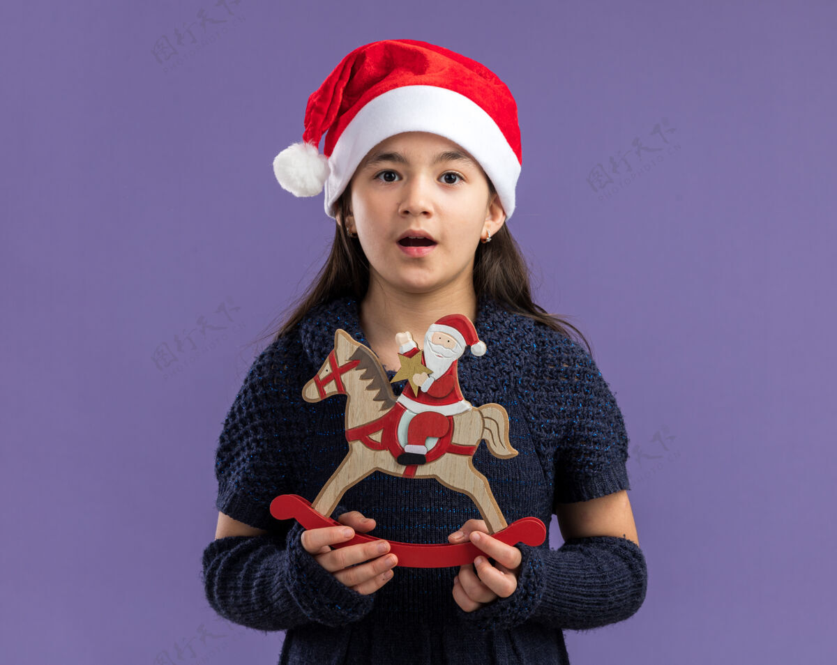 戴着小女孩穿着针织连衣裙 戴着圣诞帽 手里拿着圣诞玩具 看起来很惊讶帽子小紫色