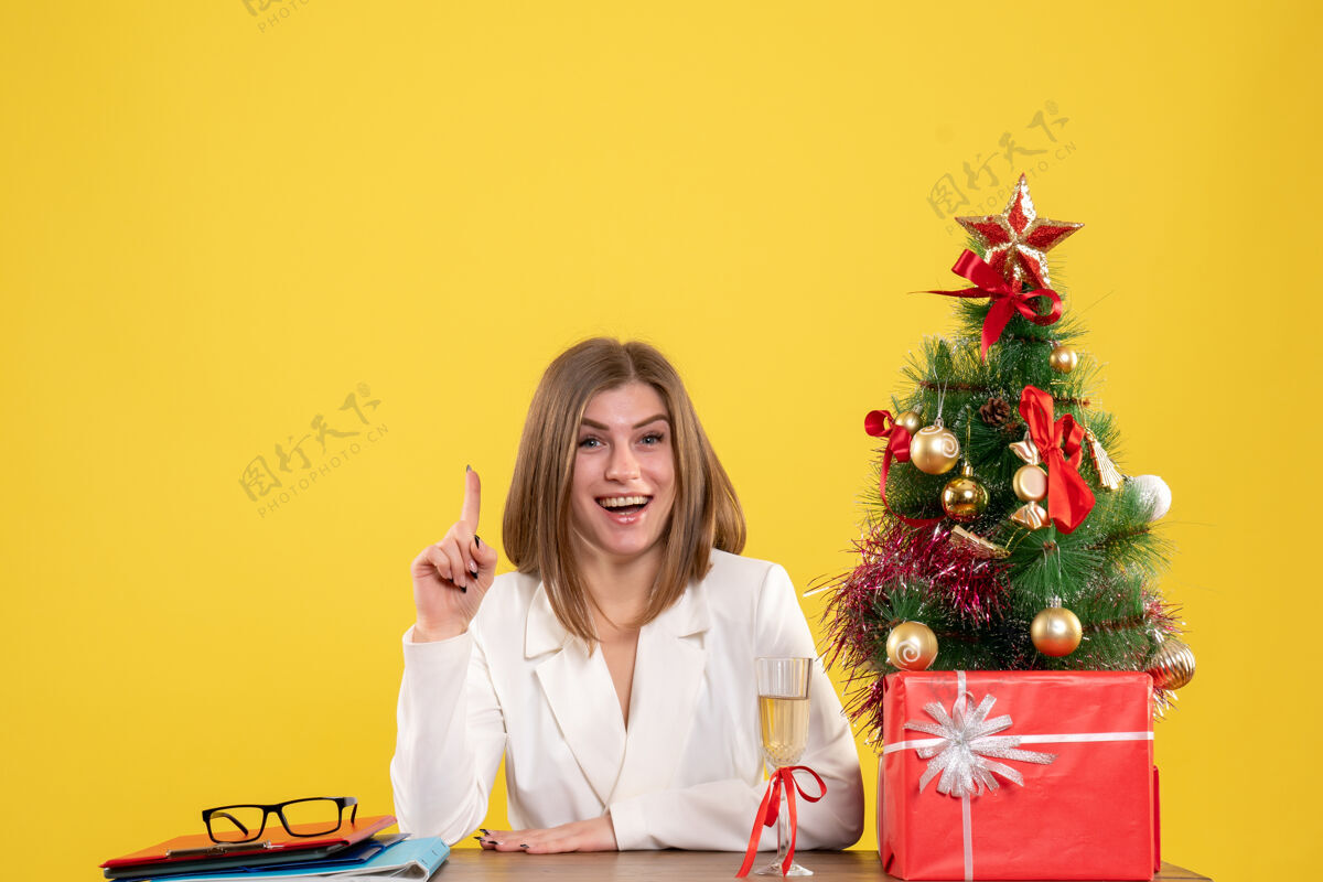 前面正面图：女医生坐在黄色背景的桌子前 放着圣诞树和礼品盒成人高尔夫女性