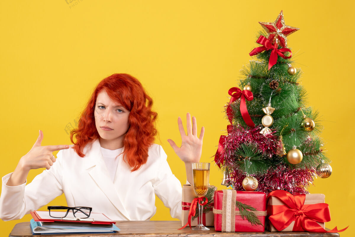 花前视图：女医生坐在桌子后面 黄色背景上有圣诞礼物快乐人插花