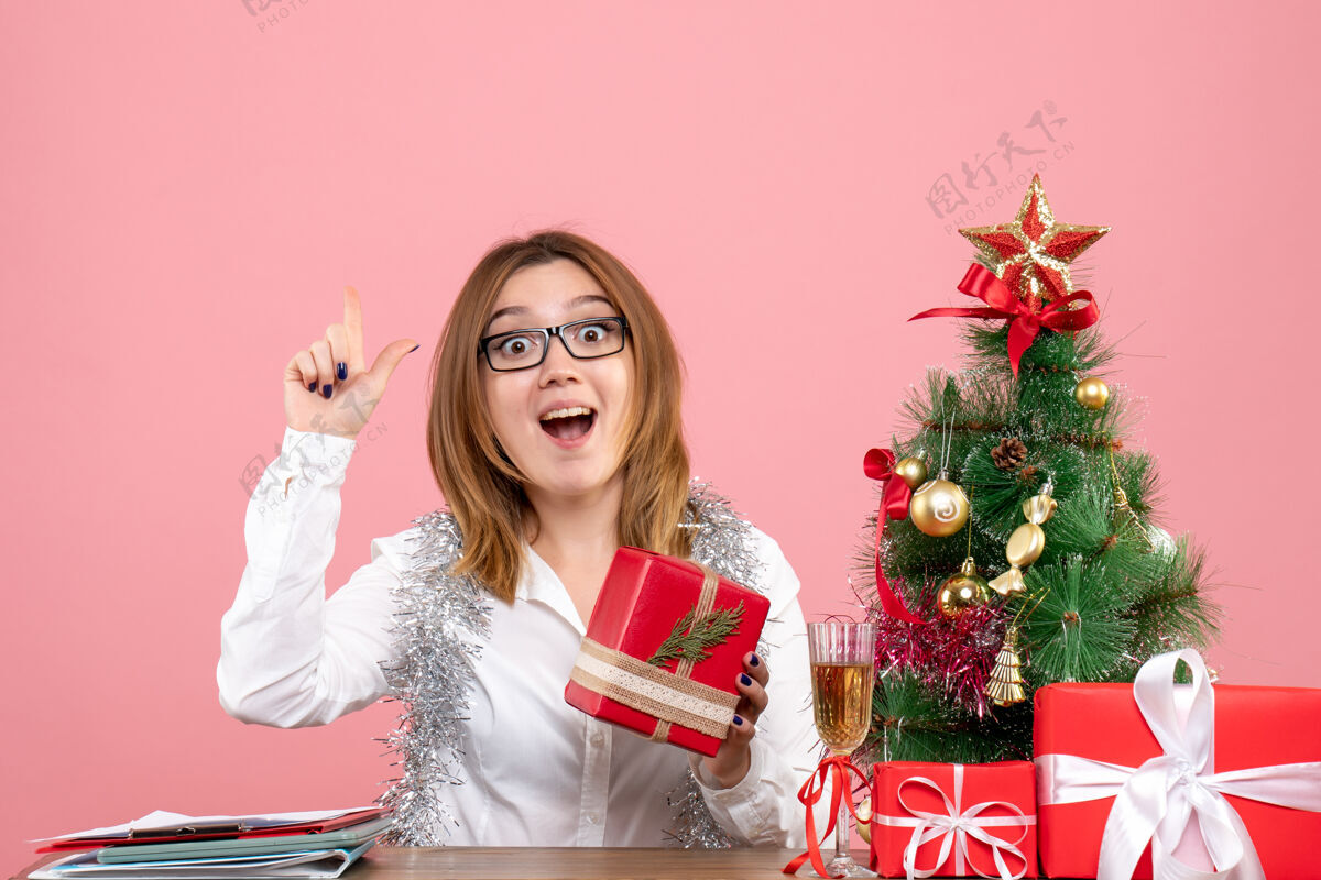 办公室女工人坐在粉红色的圣诞礼物和圣诞树旁的正视图工作坐着圣诞树