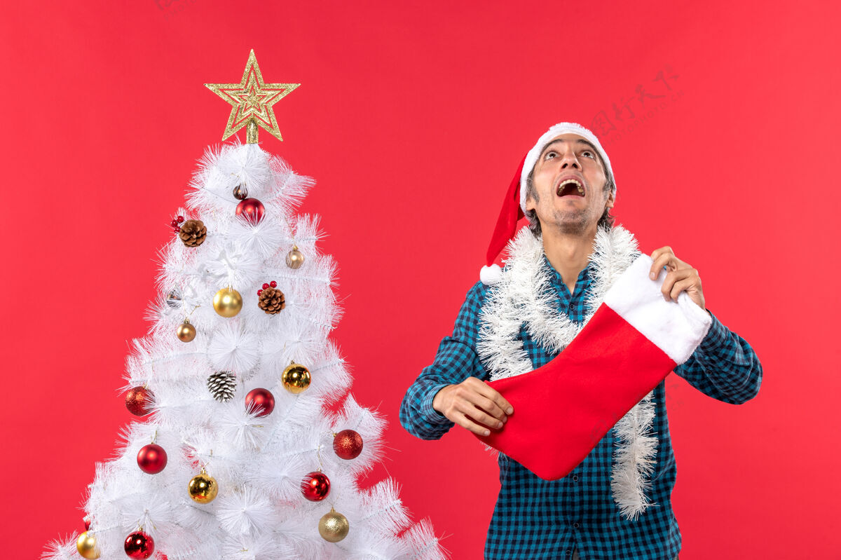 庆祝情绪激动的年轻人戴着圣诞老人的帽子 穿着蓝色的衬衫 手里拿着圣诞袜子 往上看圣诞情感衬衫
