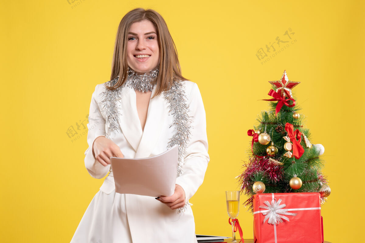 人正面图女医生站着拿着黄色背景上的文件 还有圣诞树和礼品盒衣服文件可爱