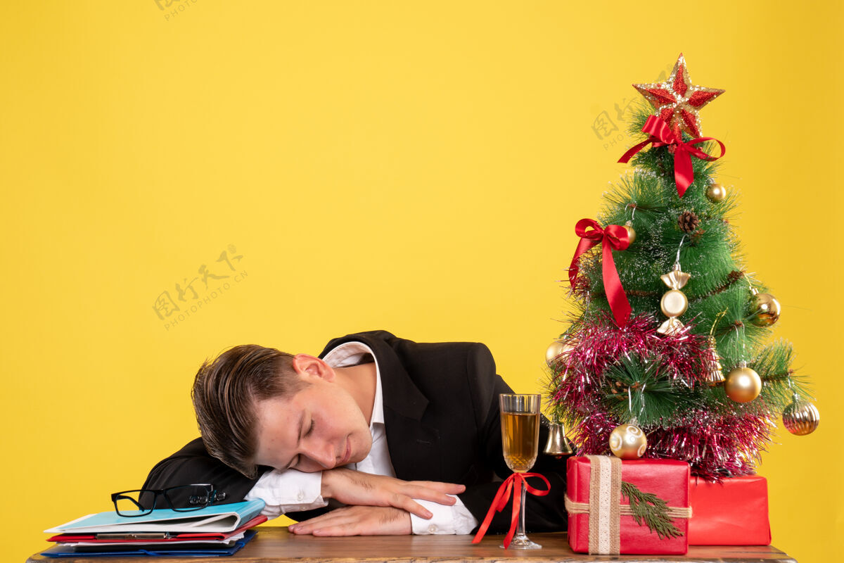 年轻男工人正面图年轻的男工人坐在圣诞礼物和树睡觉年轻人人工人