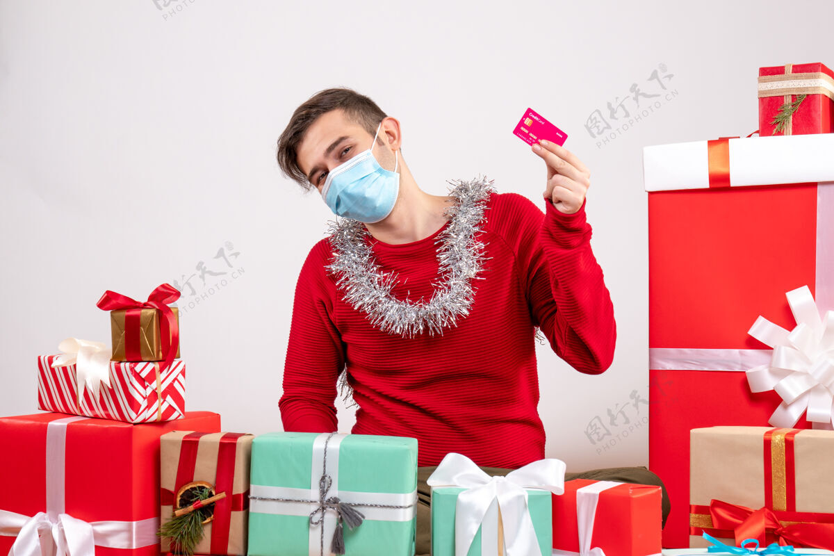 年轻正面图：戴着面具的年轻人拿着信用卡在圣诞礼物周围圣诞节男人信用