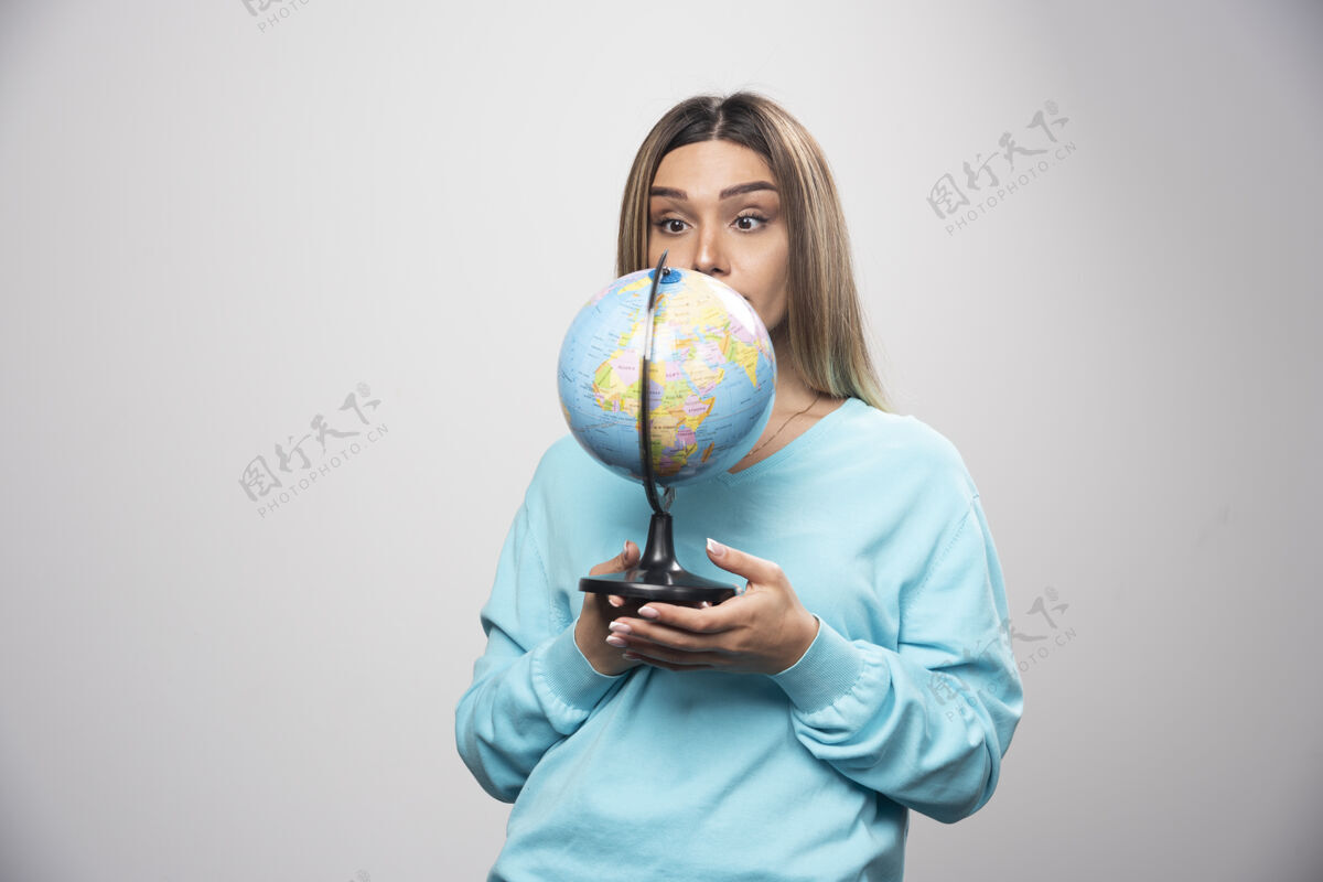 地点穿着蓝色运动衫的金发女孩拿着地球仪 看起来很惊讶旅游地理职员