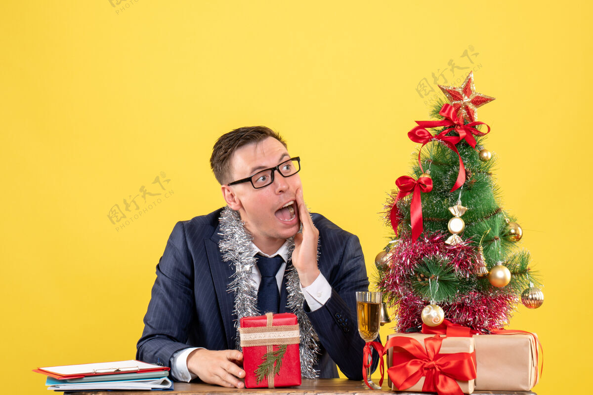 感兴趣前视图感兴趣的人在看权利坐在圣诞树附近的桌子和黄色的礼物礼物圣诞节坐着