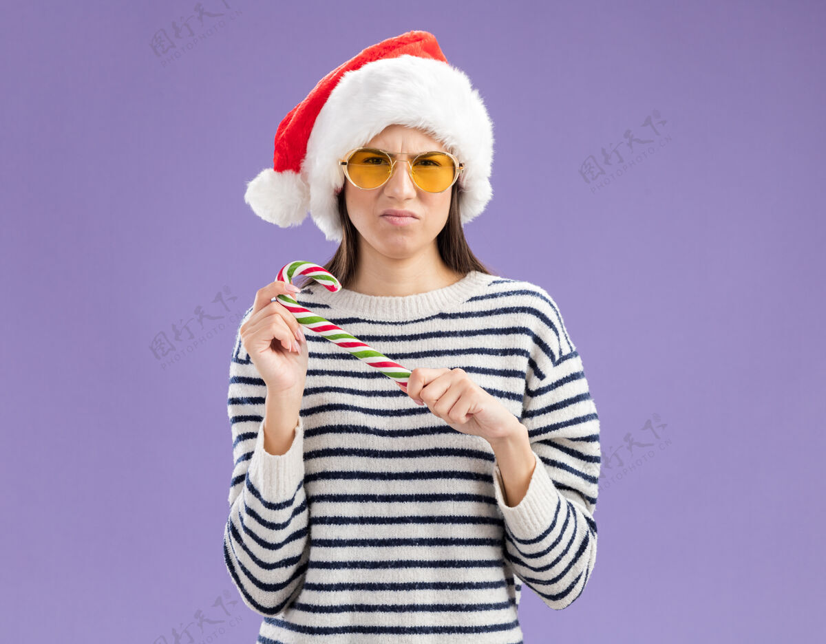 年戴着太阳眼镜 戴着圣诞帽 拿着糖果手杖的年轻白人女孩空间年轻复制