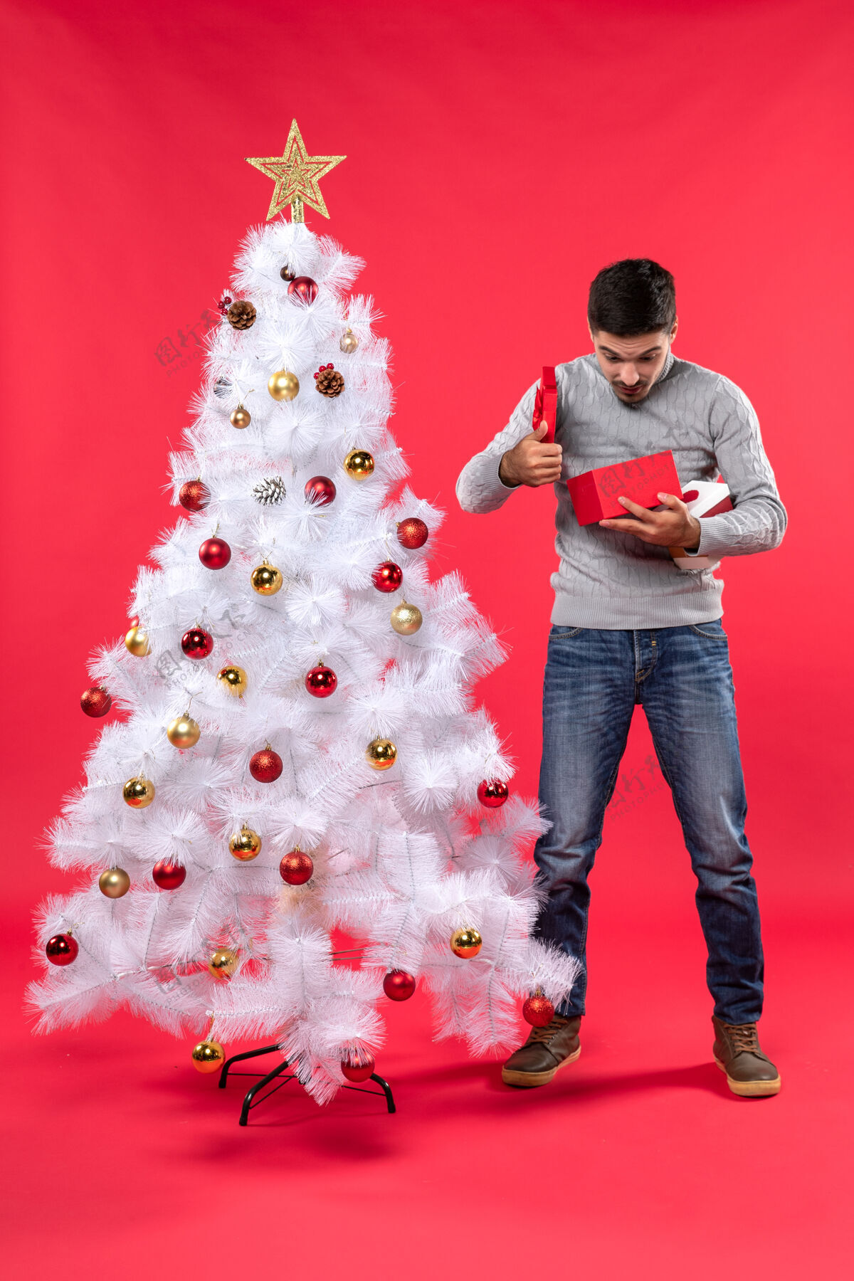 圣诞站在装饰过的白色圣诞树旁的穿着灰色上衣的帅哥大人的俯视图线站立衬衫