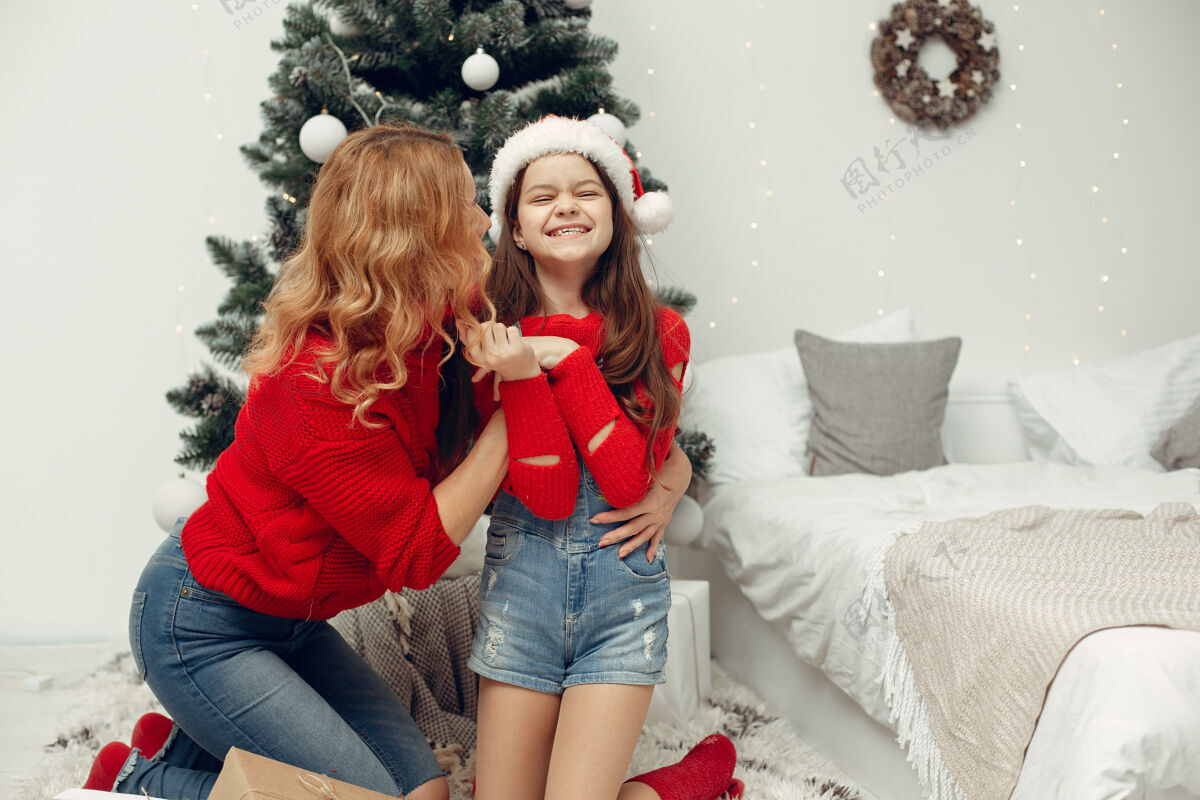 圣诞老人人们在为圣诞节做准备母亲在和女儿玩耍一家人在节日的房间里休息孩子穿着红色毛衣杉木十二月牛仔裤