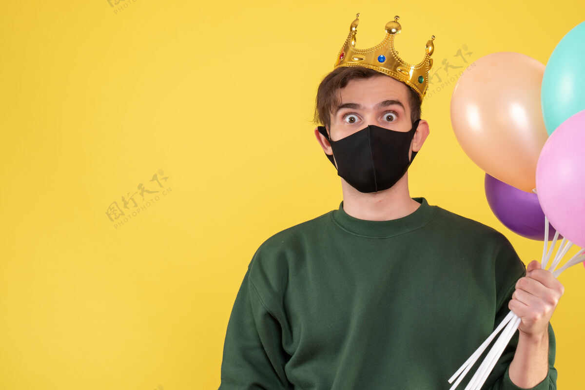 面具正面图戴着王冠 戴着黑色面具 手持黄色气球的大眼睛年轻人服装伪装脸