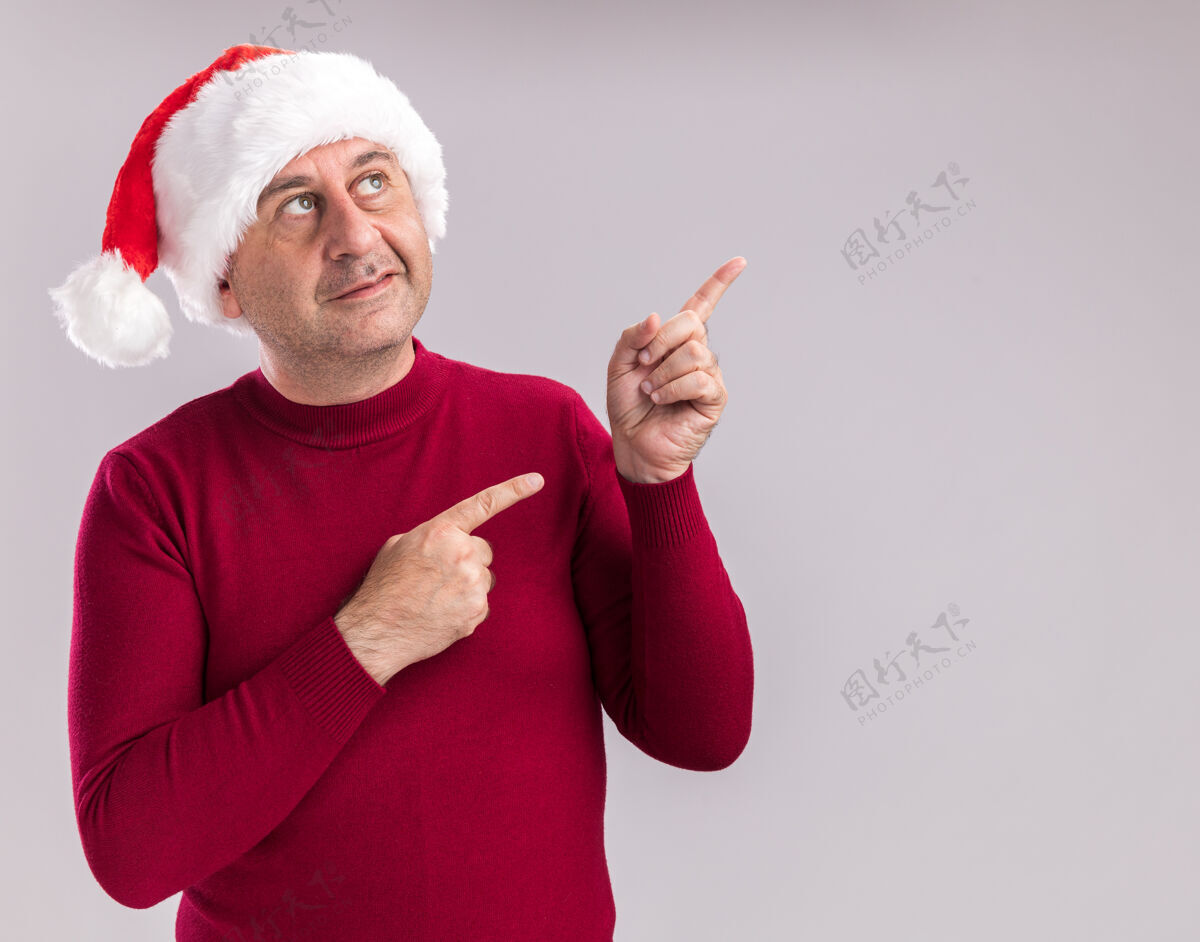 指数中年男子戴着圣诞老人的帽子 脸上挂着微笑 用食指指着站在白色背景上的一边站着脸圣诞节