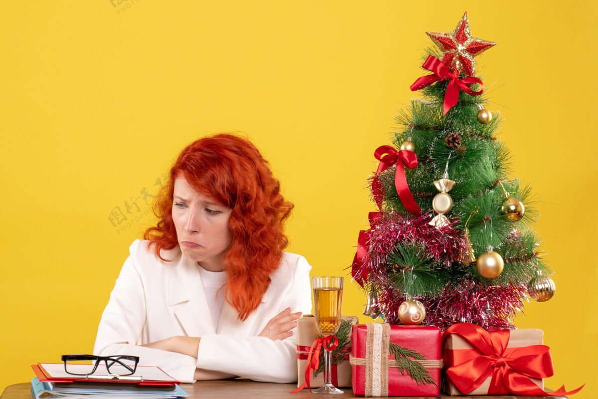 前面前视图：女医生坐在桌子后面 黄色背景上有圣诞礼物女医生医生插花