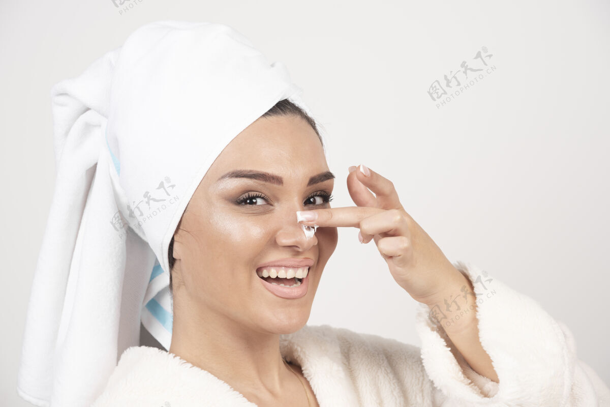 清洁穿着白色浴袍的年轻女子在鼻子上涂了一层乳霜浴袍头女孩