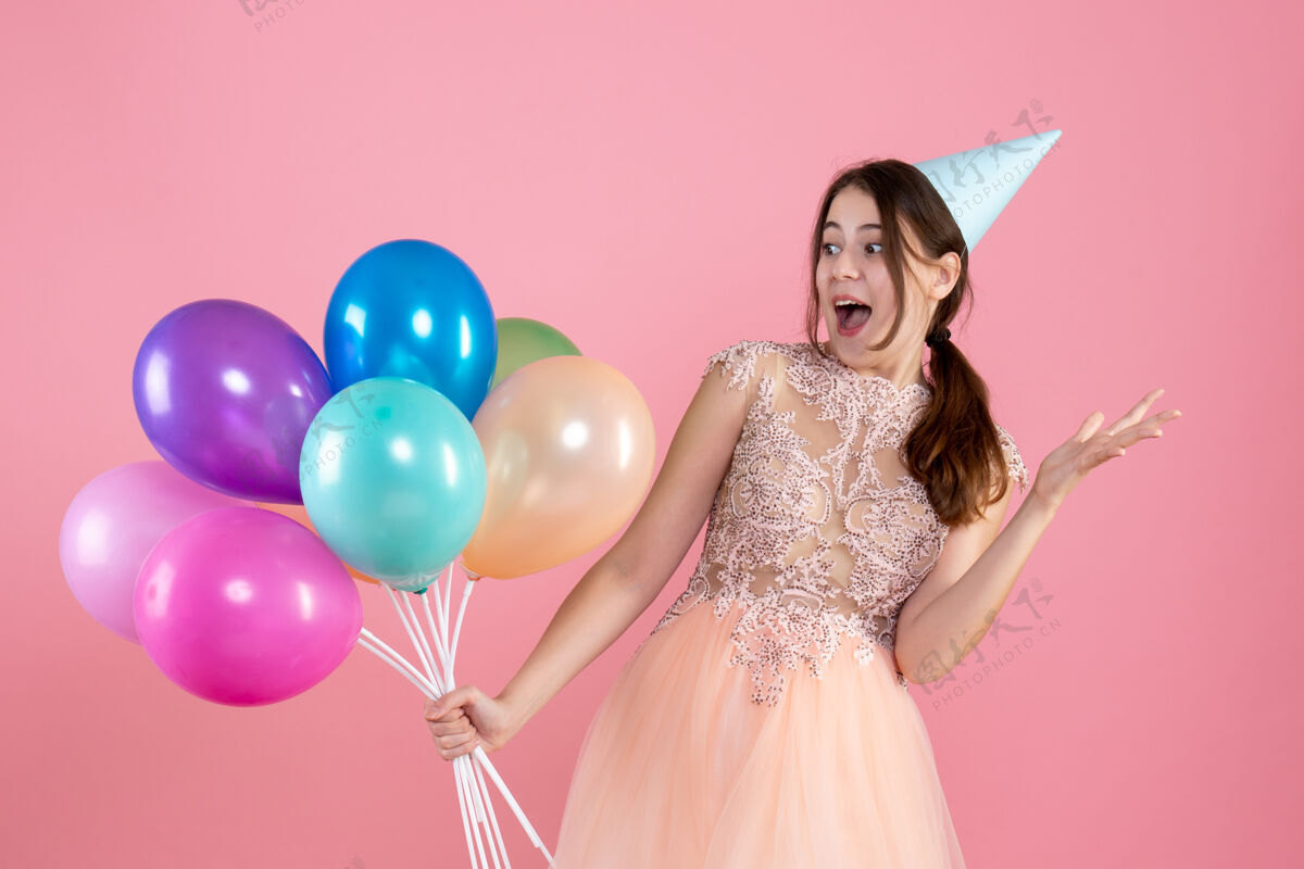 气球戴着派对帽的女孩高兴地拿着粉红色的气球庆祝贵族帽子