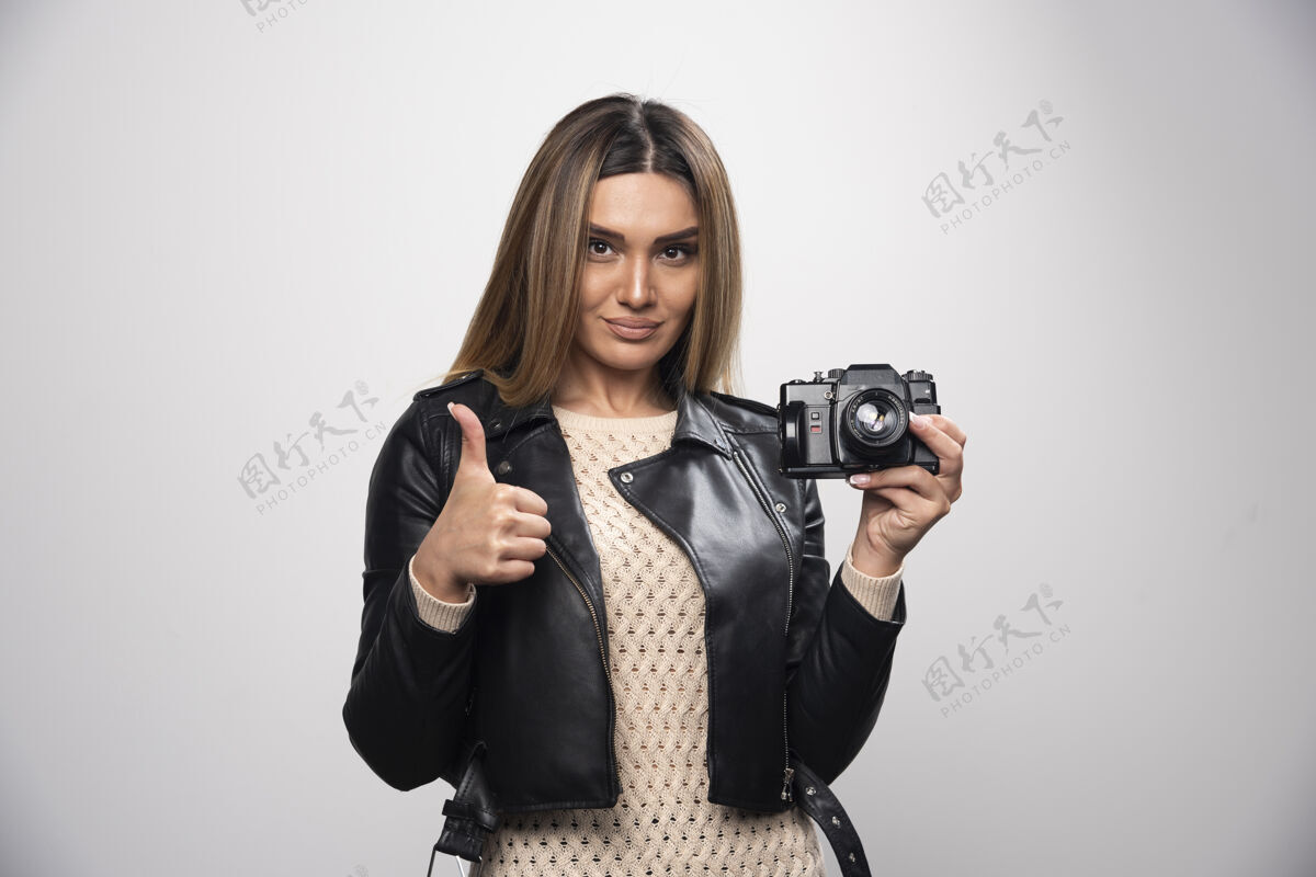 相机一位身穿黑色皮夹克的年轻女士 以积极微笑的态度用相机拍照人类数码姿势