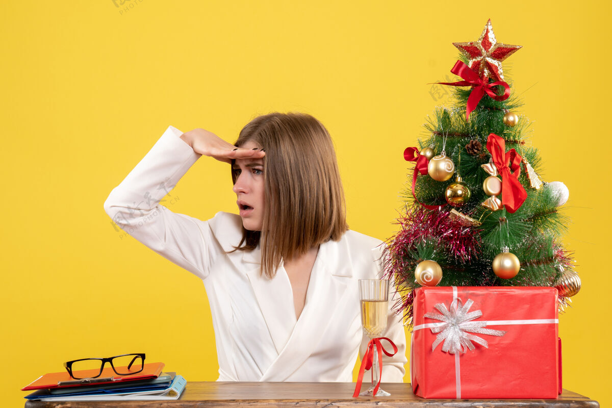 成人正面图：女医生坐在黄色背景的桌子前 放着圣诞树和礼品盒桌子生活人