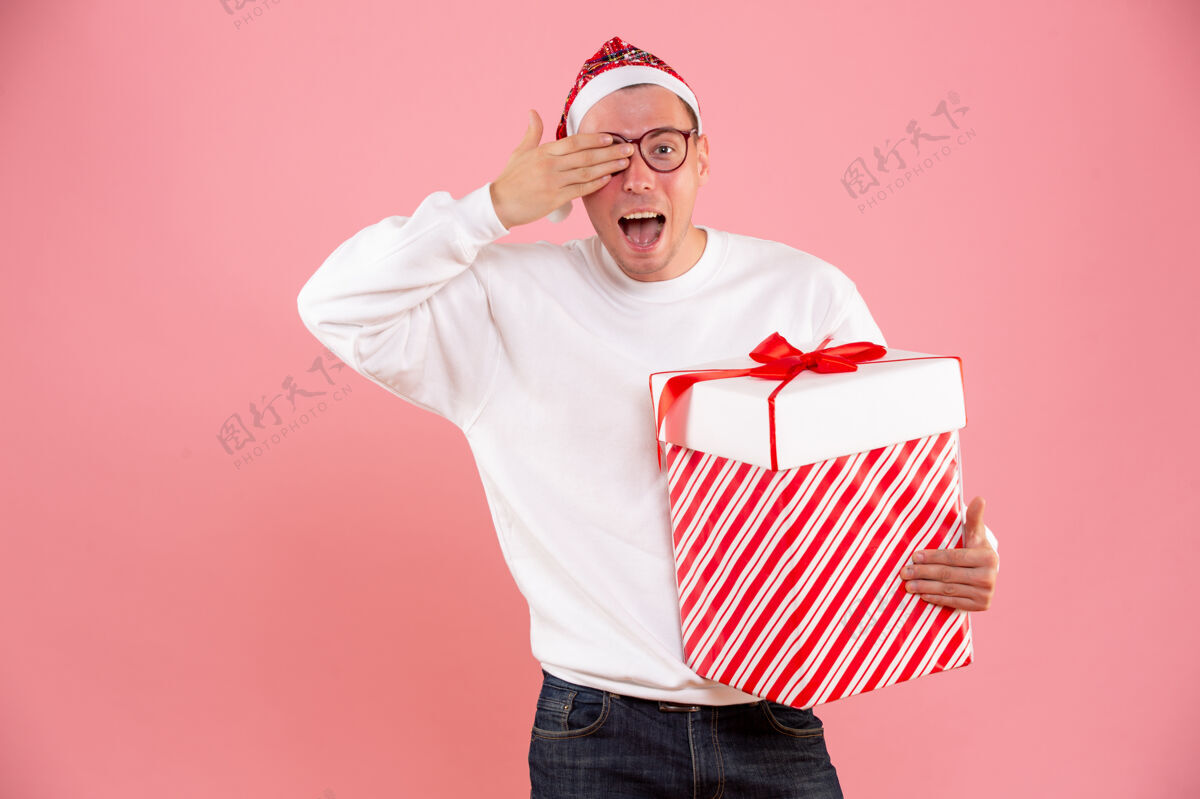 庆祝一个年轻人拿着大礼物在粉红色墙上的前视图十二月微笑礼物