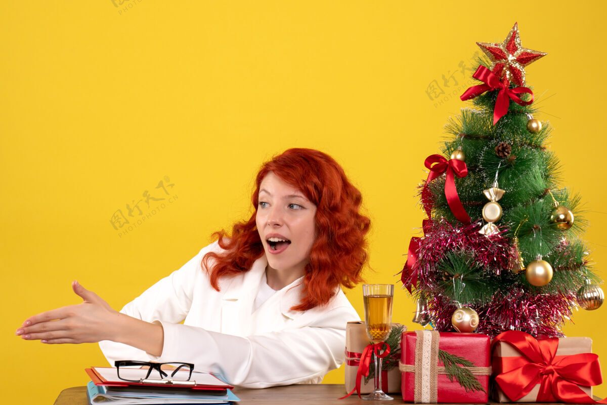 人女工人坐在桌子后面 手里拿着圣诞礼物和黄色的圣诞树工人成人黄色