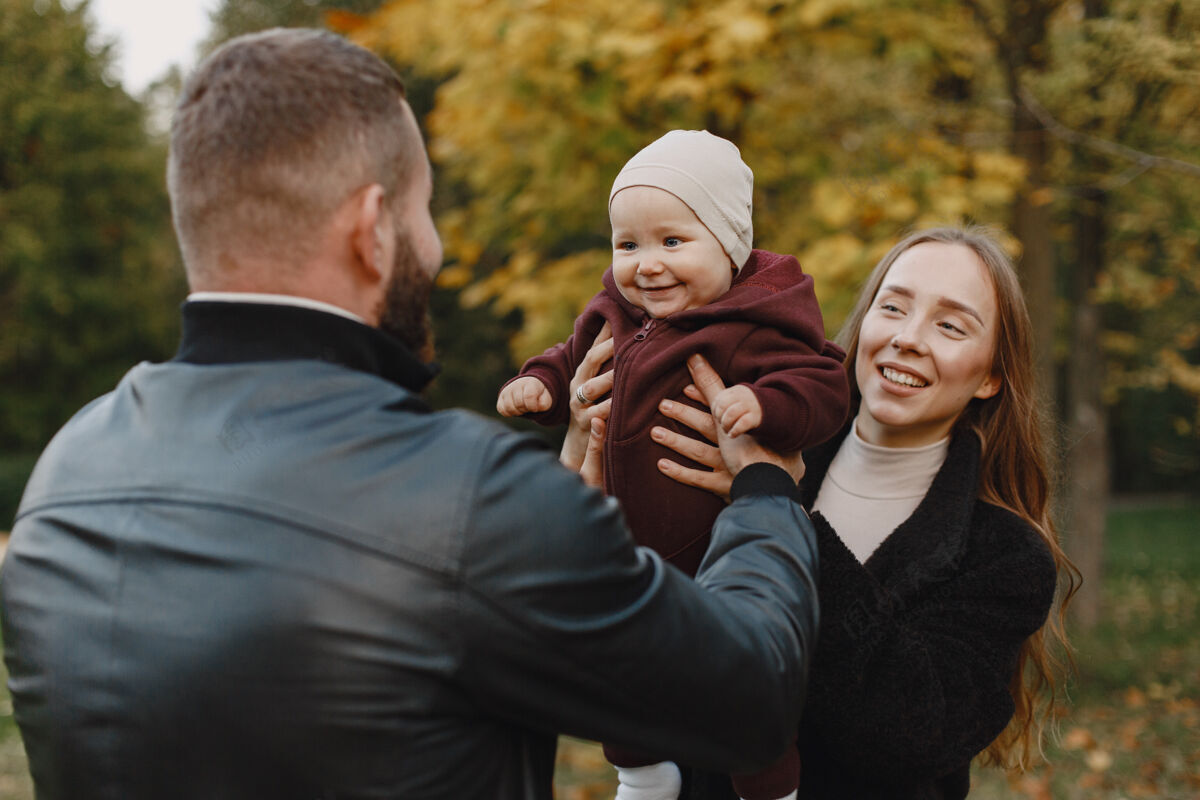 户外一家人在秋天的公园里男人穿着黑色夹克可爱的小女孩和父母公园母亲女人