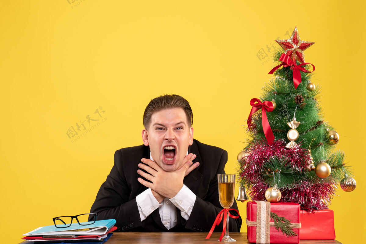 坐着前视图年轻的男工人坐在圣诞礼物和圣诞树情感颜色执行官