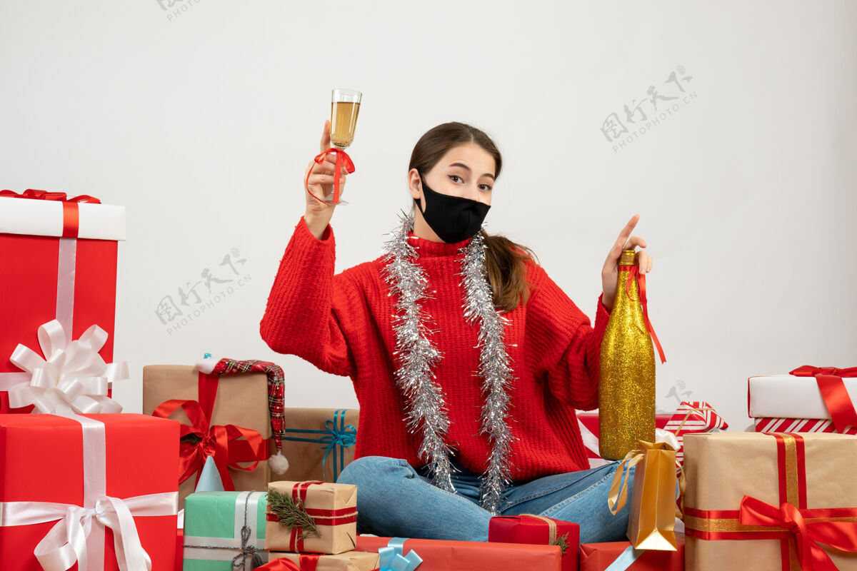 成人戴着黑色面具的年轻女孩拿着香槟瓶 围坐在白色的礼物旁敬酒人面具包