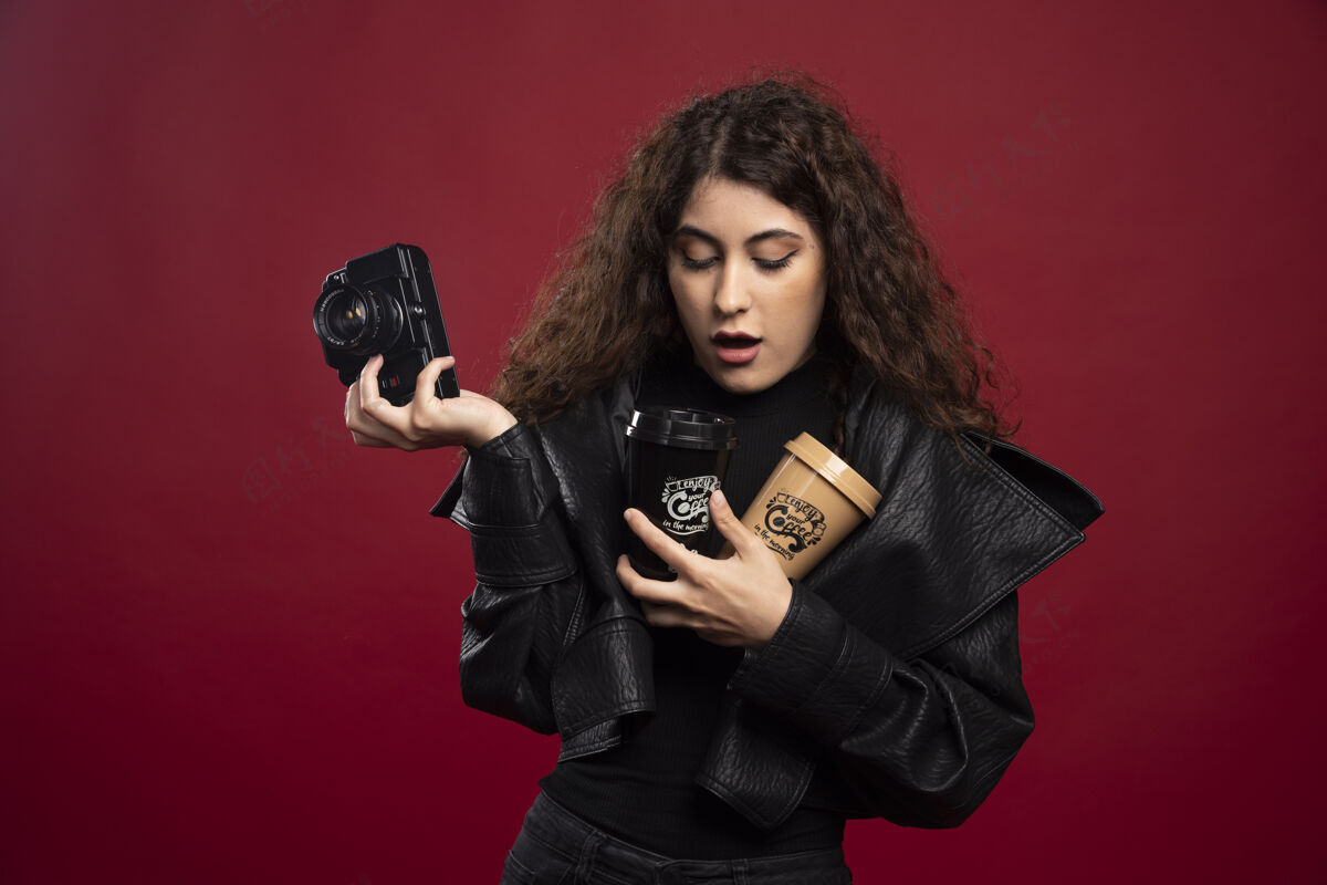 咖啡杯一个穿着全黑衣服的年轻女人手里拿着一个杯子和一个照相机外卖相机装束
