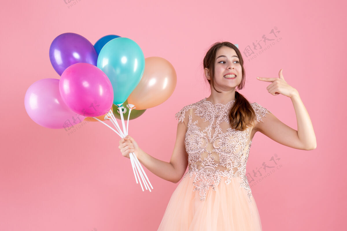 贵族戴着派对帽的派对女孩拿着气球指着粉色的笑容粉红色女孩党的女孩