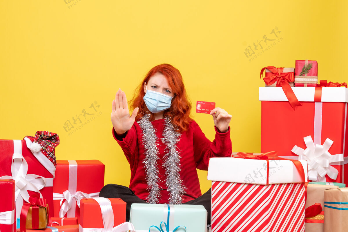 银行正面图是一位年轻女子戴着面具围坐在礼物旁边 黄色的墙上挂着银行卡前面年轻人圣诞节