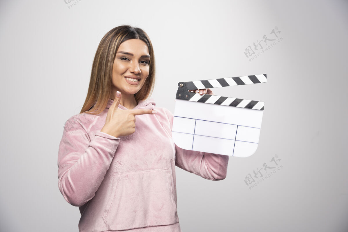 女性穿着粉色运动衫的金发女士拿着一块空白的隔板 摆出自然的姿势电影电影拍板