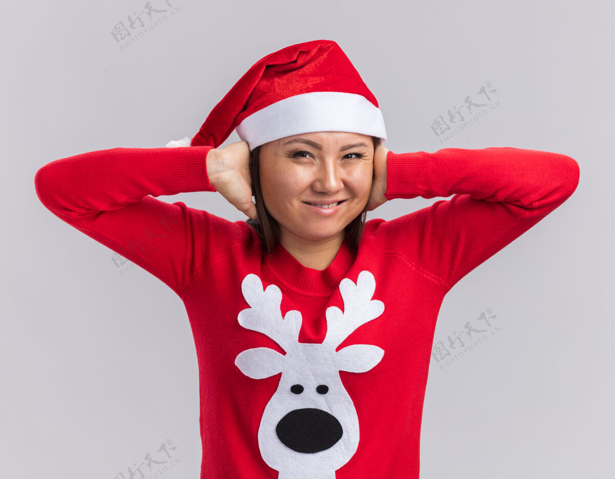 女孩恼怒的亚洲小女孩戴着圣诞帽 戴着毛衣 耳朵被隔离在白色背景上毛衣圣诞节耳朵