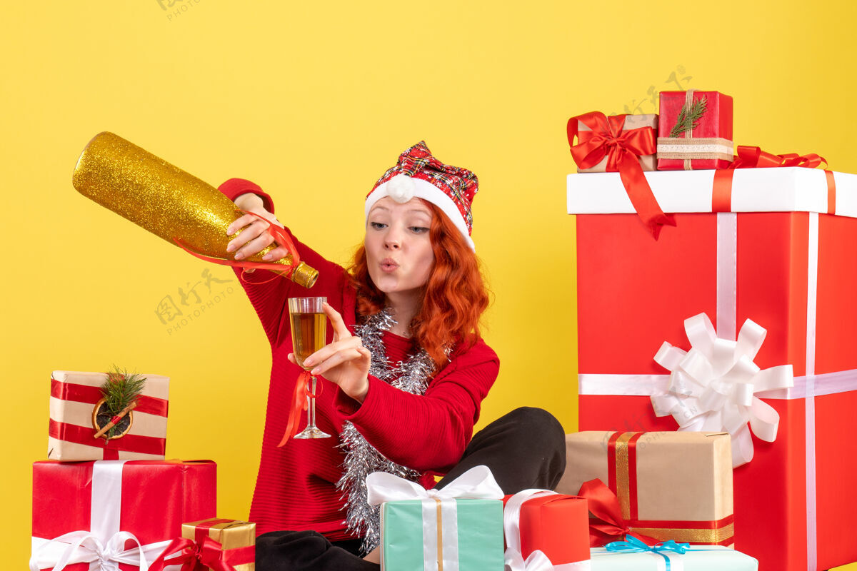 人年轻女子围坐在圣诞礼物旁 在黄色墙壁上用香槟庆祝的正面视图圣诞节年轻音乐家