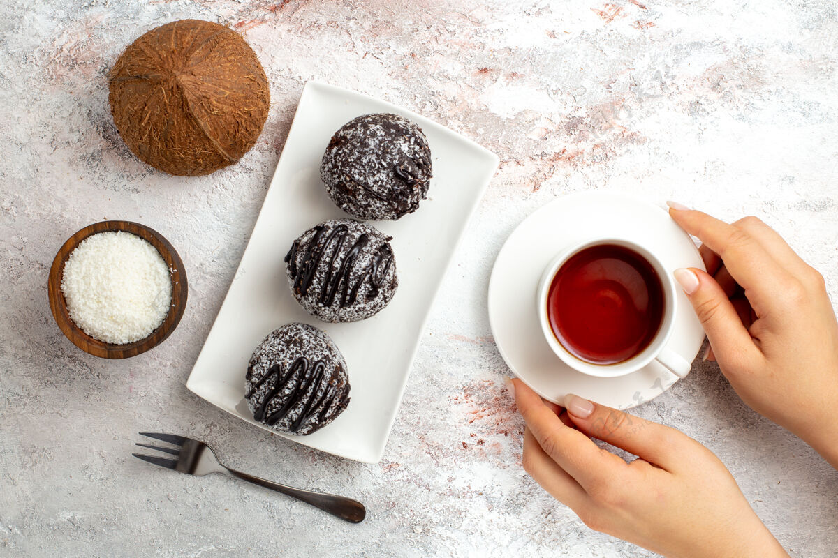 马克杯俯瞰巧克力蛋糕与一杯茶和椰子的白色表面巧克力蛋糕饼干糖甜饼干杯子巧克力视图