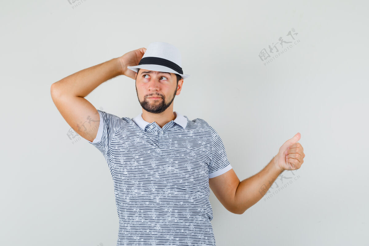 手势年轻人穿着t恤 戴着帽子 大拇指指向侧面 面带沉思 俯视前方帽子休闲成人