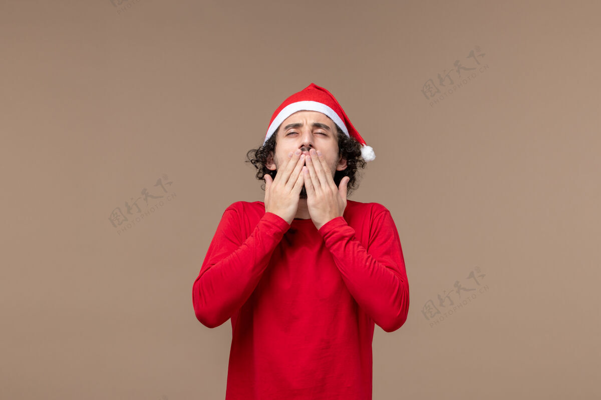 表情正面图：一个穿着红色圣诞斗篷的年轻人 背景是棕色的圣诞节红色艺人喜剧演员