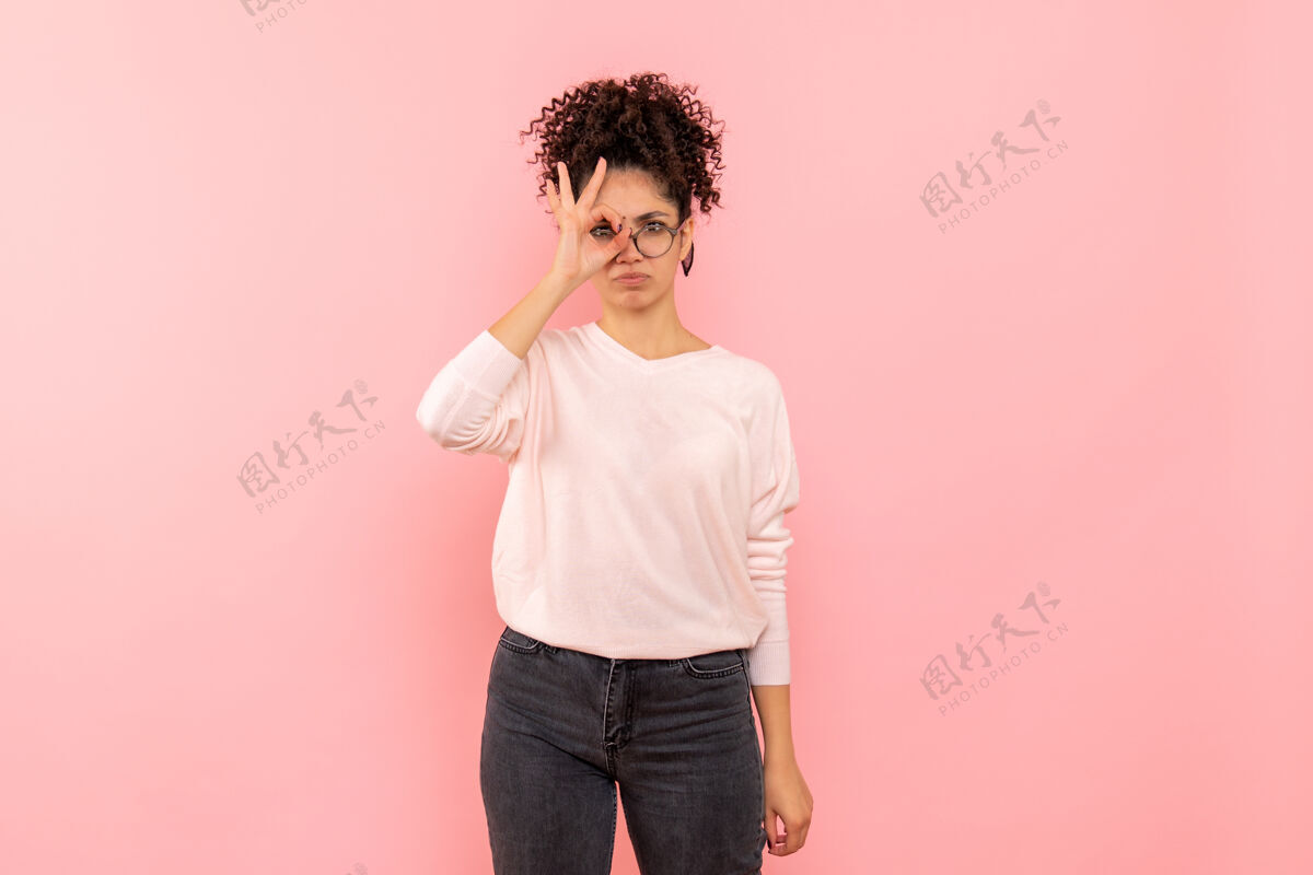 看年轻女子透过手指在粉红色墙上看的前视图站模特女性