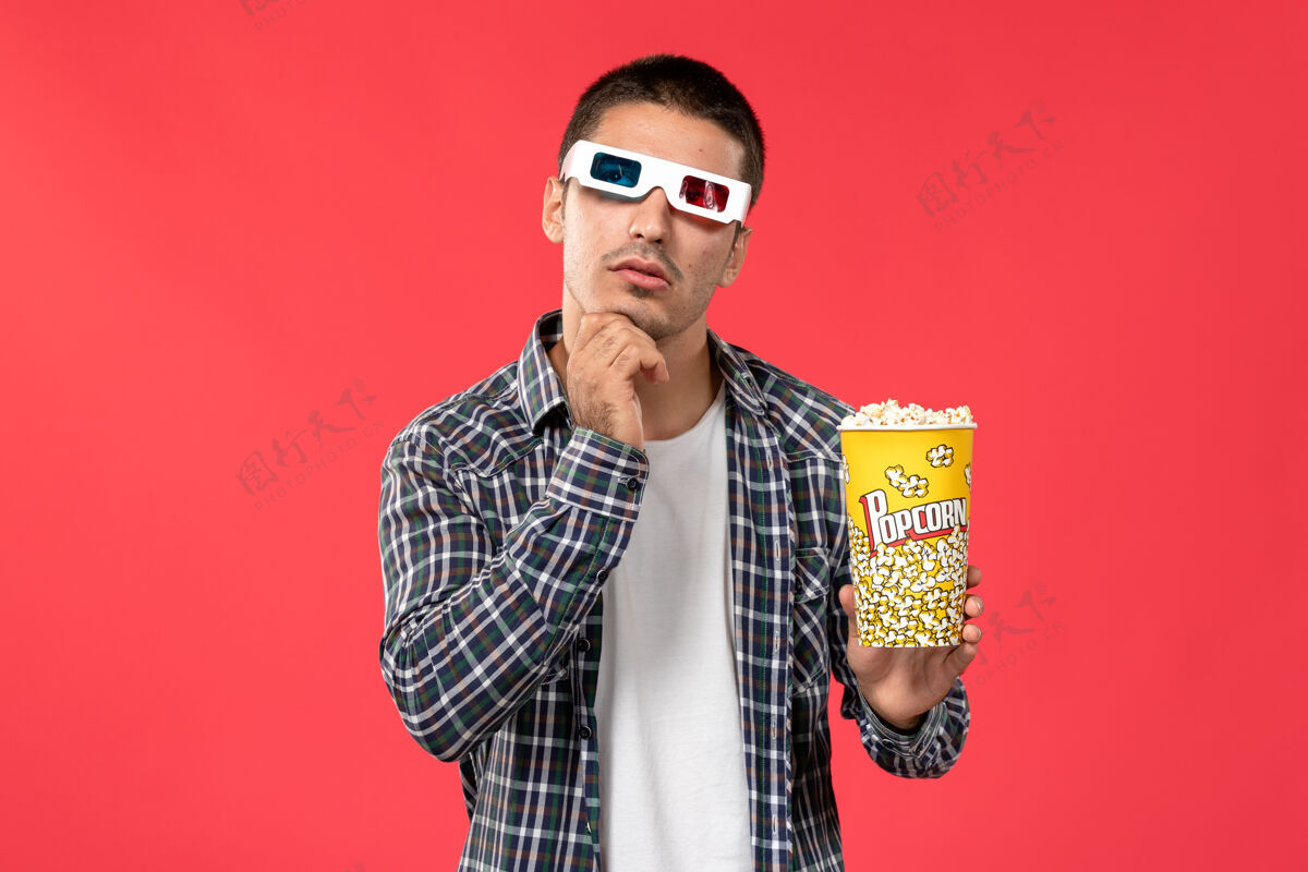 男性正面图年轻男子拿着爆米花包在-d太阳镜上思考着淡红墙电影院的电影浅红色肖像剧院