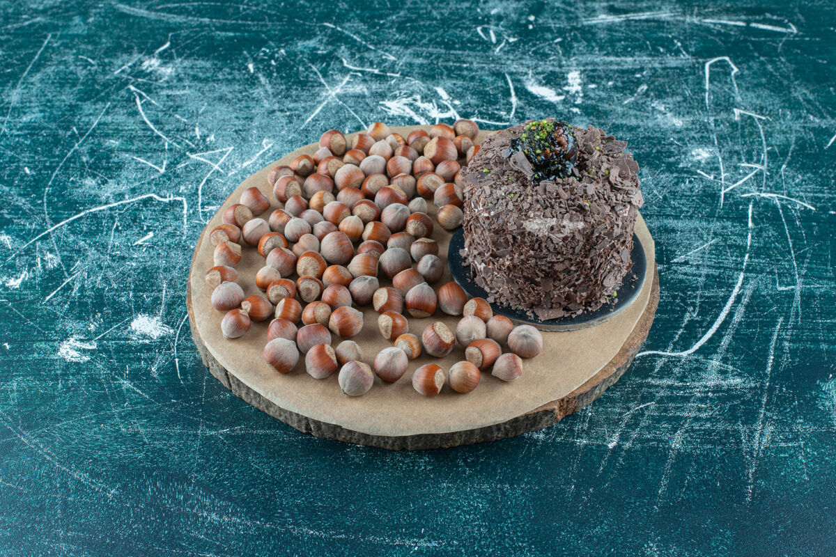 美味一堆榛子 旁边是一块小蛋糕 放在蓝色的木板上甜品巧克力水果