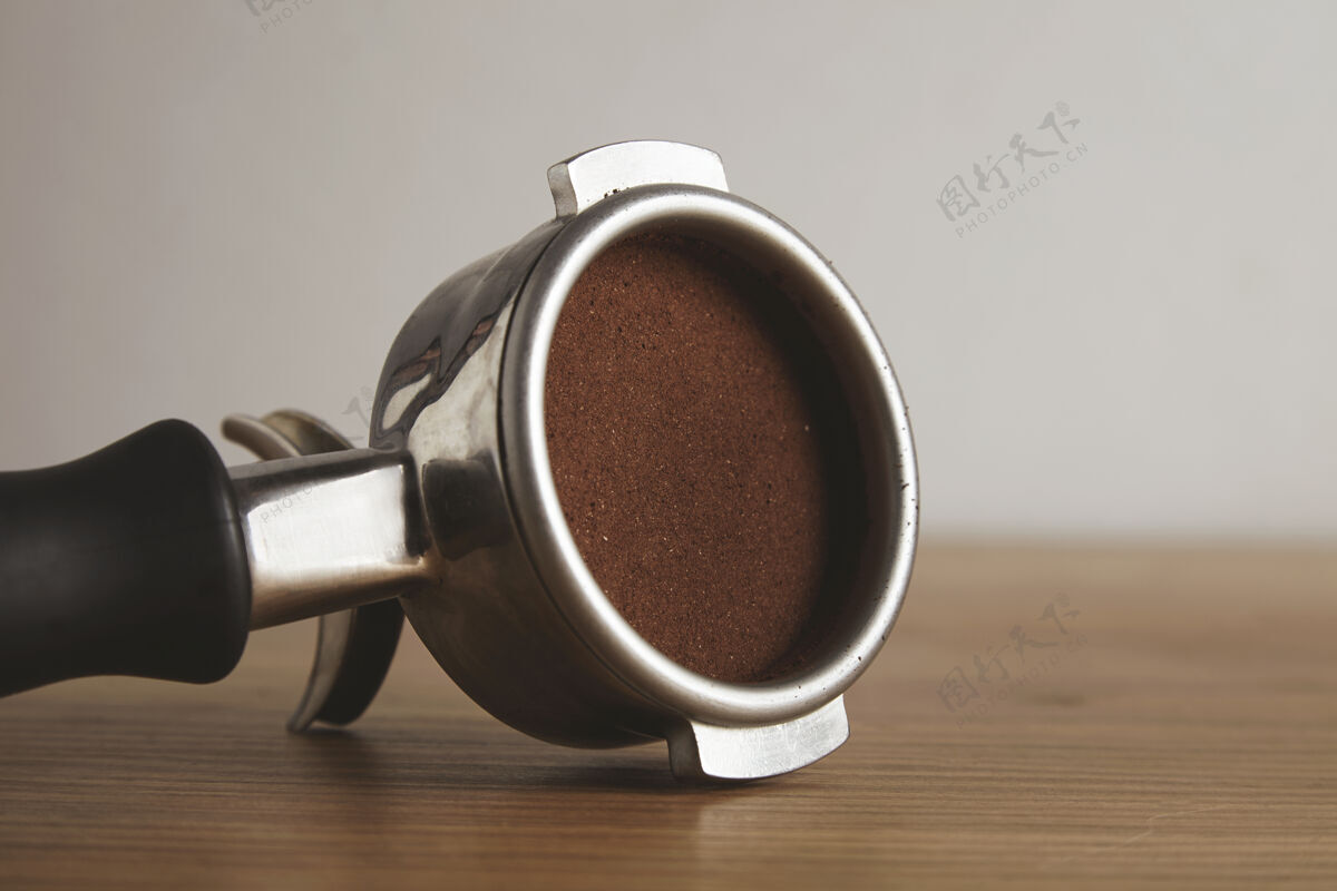 杯子特写在钢制的便携式过滤器上 里面压着磨碎的咖啡粉在咖啡厅的木桌上隔离专业的咖啡酿造机器咖啡厅热的