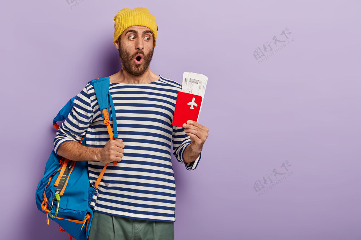 国外度假和旅游的概念惊讶的未刮胡子的家伙摆出背包在肩膀上困惑背包客机票