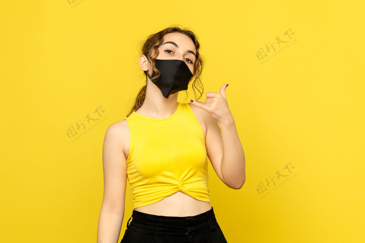 人黄色墙壁上戴着无菌口罩的年轻女孩的正视图漂亮时尚流行病