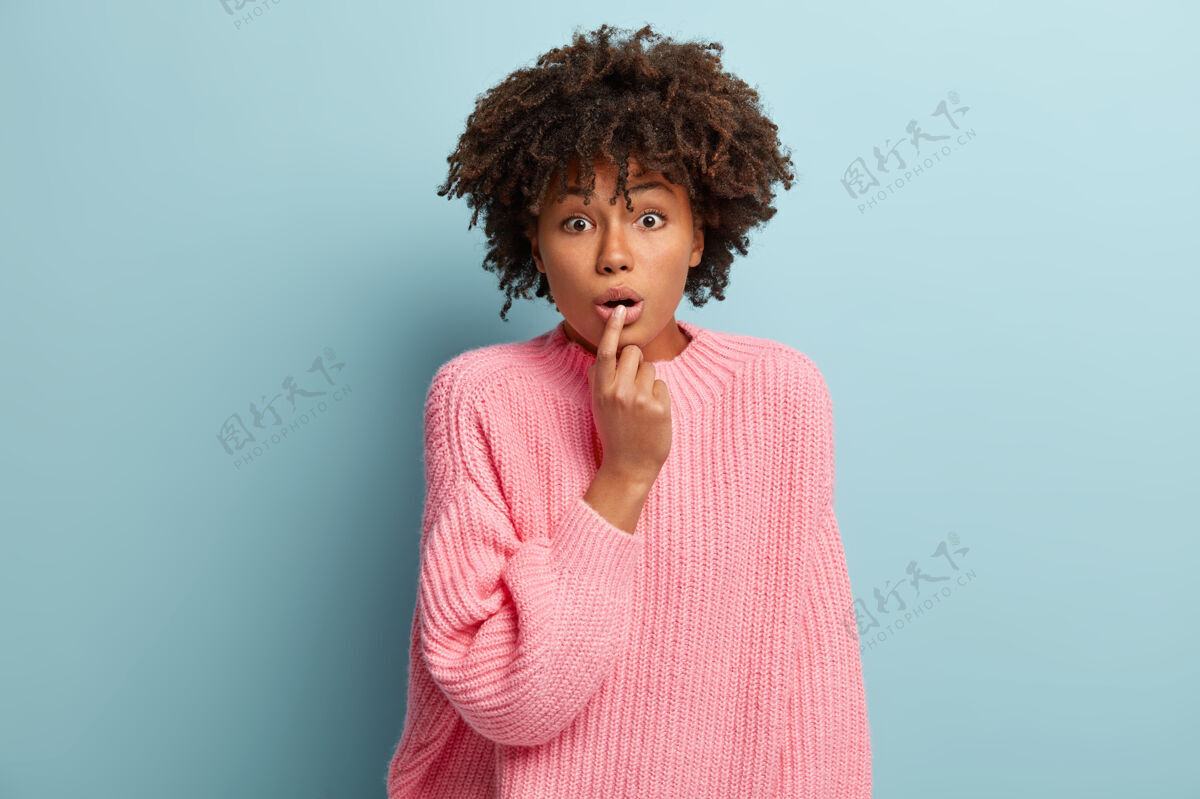 印象深刻震惊的非洲裔美国女士的画像惊讶地喘气 手指放在嘴唇上 无言以对 听着有点担心的表情 穿着粉色的套头衫 模特室内天哪震惊可怕种族