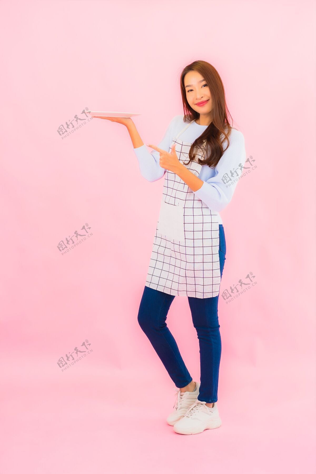 新鲜肖像美丽的亚洲年轻女子在厨房穿着围裙在粉红色的隔离墙上工人烹饪美食