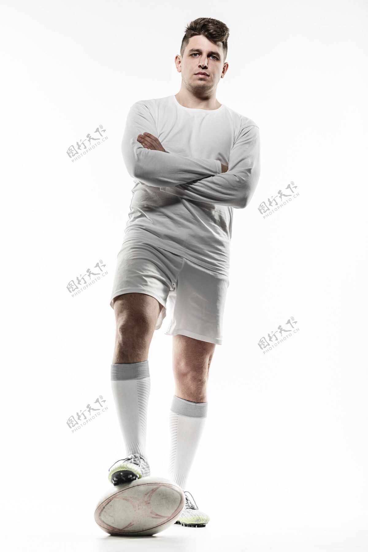 锦标赛前视图的男性橄榄球运动员摆姿势与球和双臂交叉联盟垂直足球