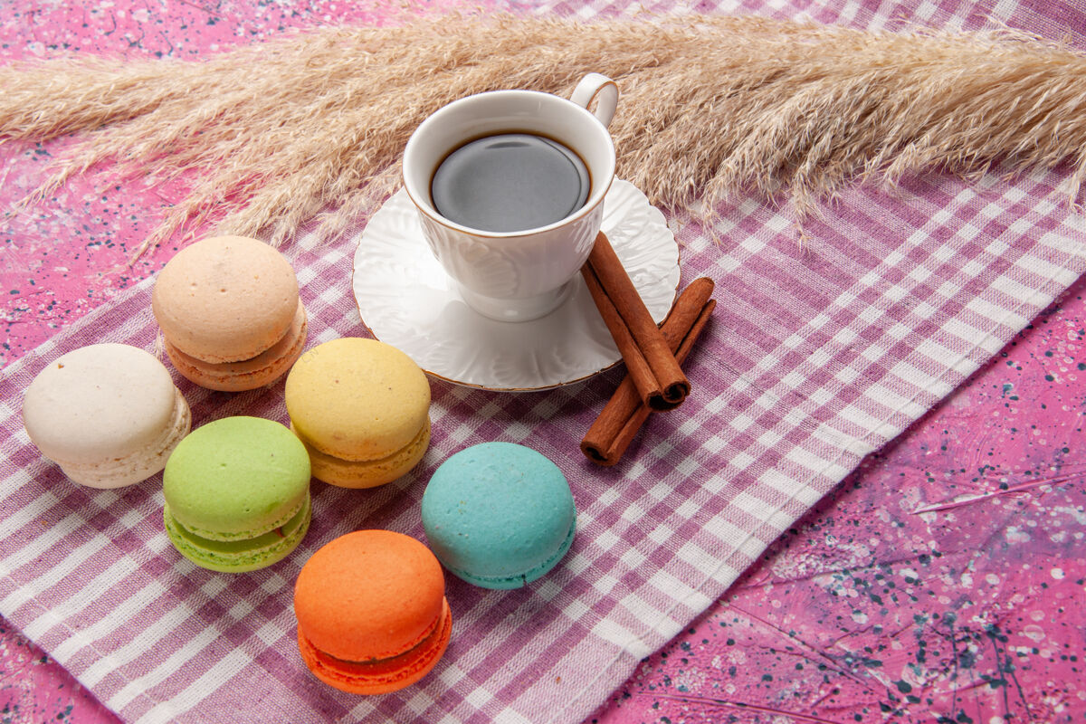 生的一杯茶加肉桂和法式马卡龙放在粉红色的桌上蛋糕饼干甜甜的糖杯子筒子麦卡龙