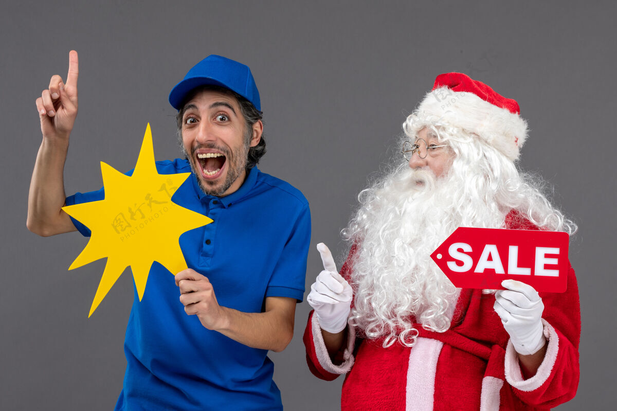 男人圣诞老人的正面图 男性信使手持销售横幅 灰色墙上有黄色标志快递前面举行