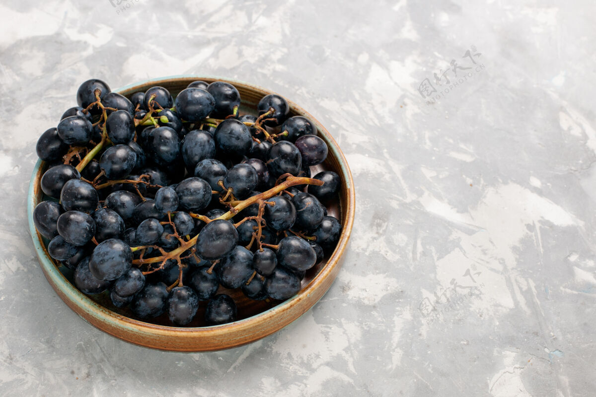 酒正面是新鲜的黑葡萄 多汁 醇厚 甜甜的水果 浅白的桌子 水果 新鲜 醇厚的果汁 葡萄酒可食用的水果蓝莓葡萄