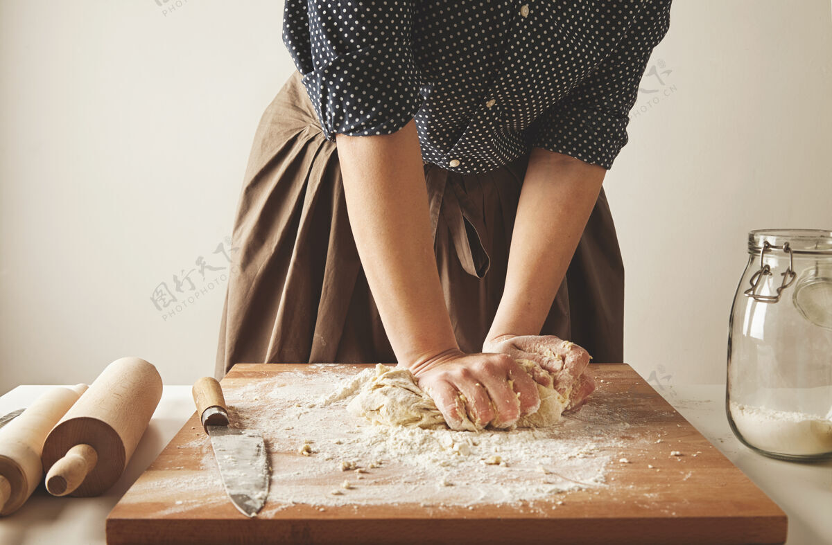 传统女人在两个擀面杖和面粉罐旁的木板上揉面团手工制作烹饪准备